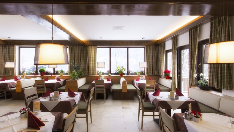 Interior view of a cozy restaurant with wooden furniture, laid tables and large windows.