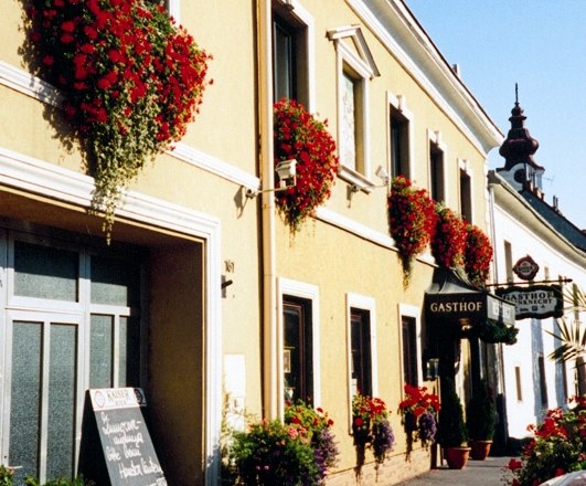 house, © Gasthof Weinknecht A traditional inn with a yellow façade and red flowers on the windows.