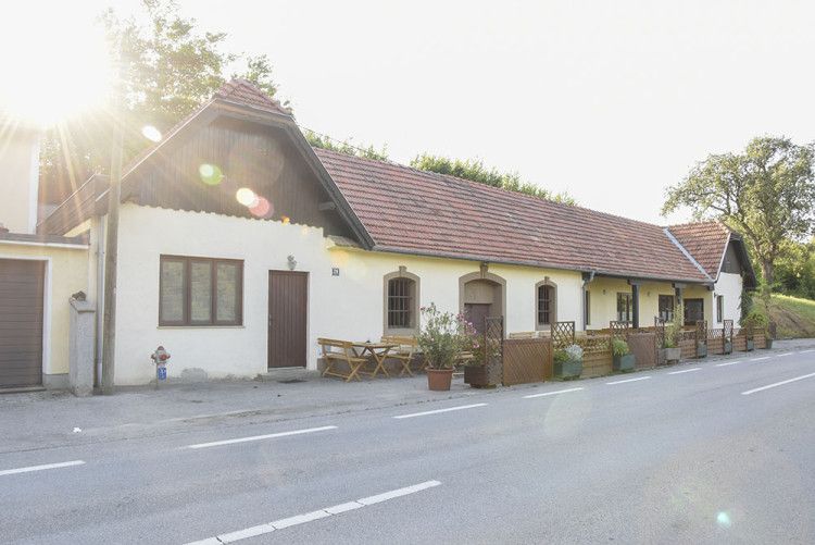 A traditional building with red tiled roofs and wooden tables in front of the door, illuminated by the sun.