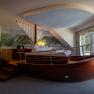 Hotel room with bed in the shape of a boat, wall painting of landscape, window with curtains.