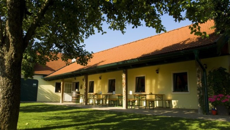 A Heurigen garden with a yellow building, red roof tiles and a green meadow.