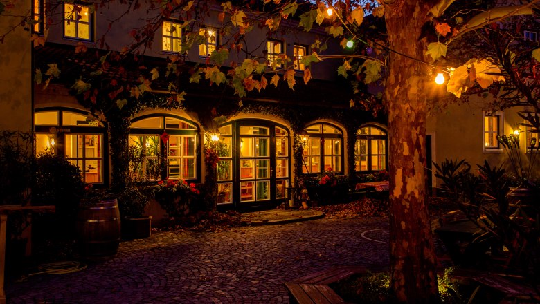 Cozy inner courtyard of a building at night, illuminated by warm light and surrounded by autumnal trees.