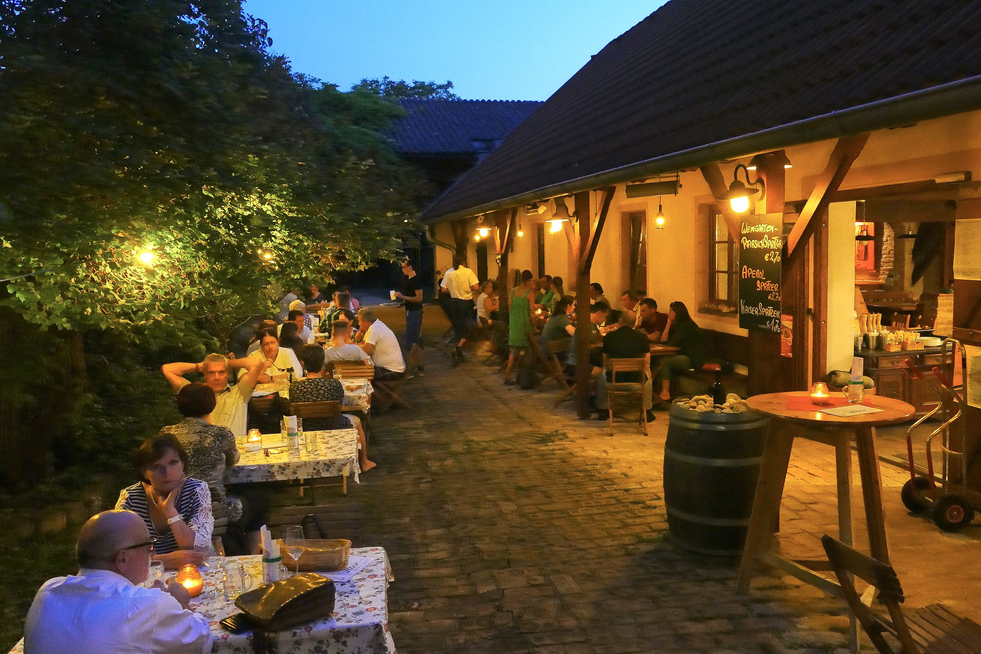 People sitting in a cozy outdoor area of a Buschenschank (typical tavern) in the evening.