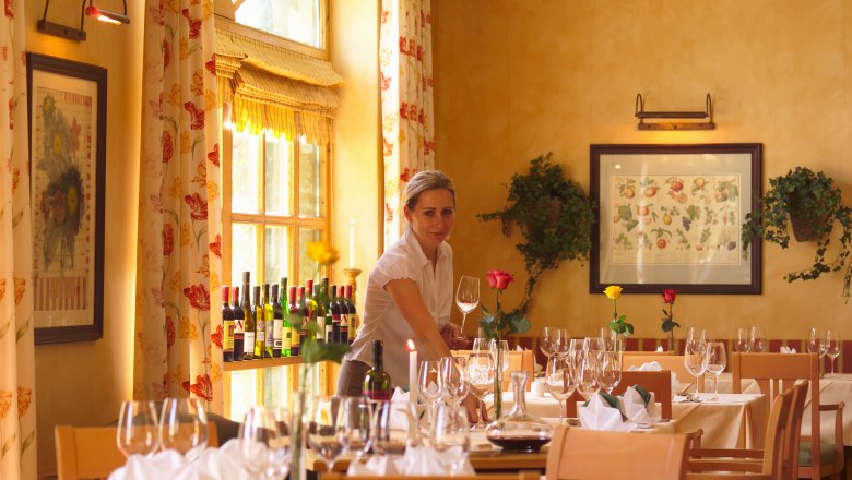 A woman sets tables in an elegant restaurant with wine glasses and flowers.