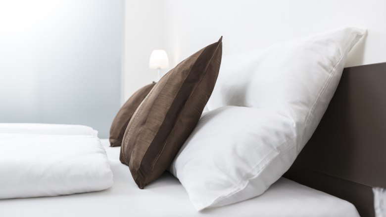A bed with white cushions and brown decorative pillows, a lamp in the background.