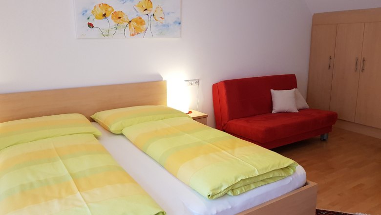 A double room with a bed, a red sofa, a wardrobe and a picture on the wall.