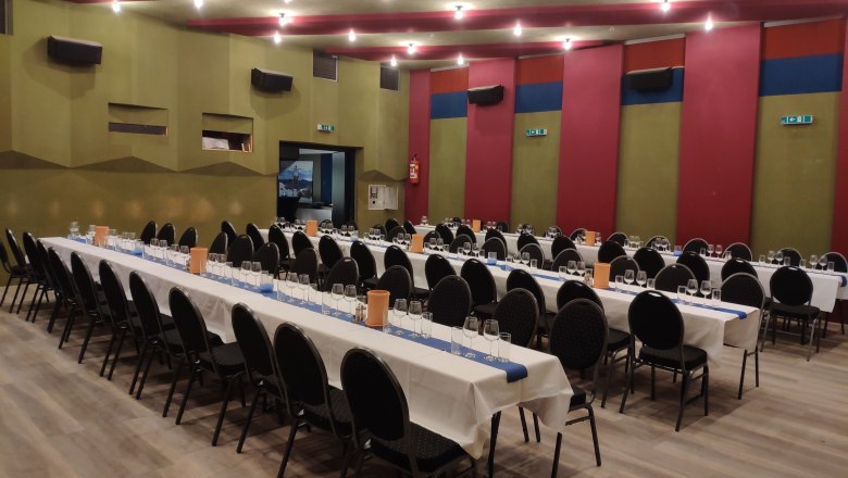 A large hall with long, laid tables and black chairs, ready for an event.