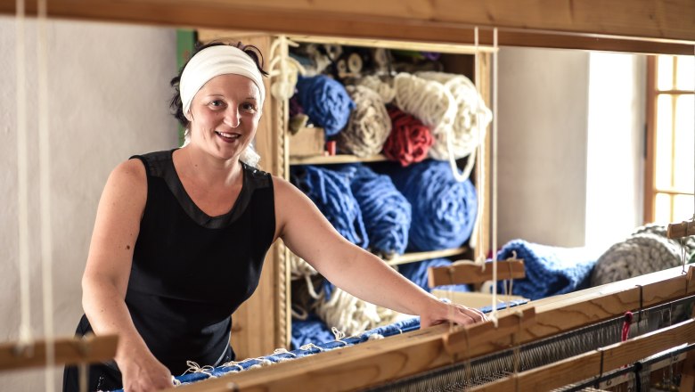 Woman at the loom with balls of wool in the background.