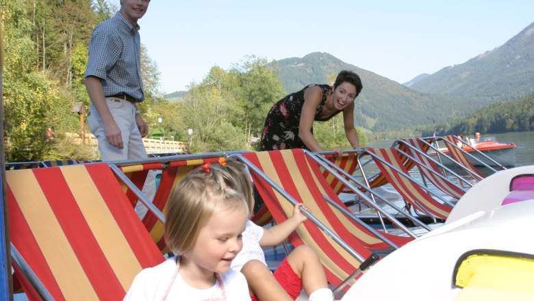 Family with children on pedal boats on a lake with mountains in the background.