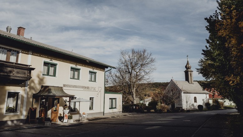 Inn and church in Steinbach near Nagelberg, surrounded by trees and blue sky.