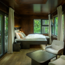 Interior view of a modern tree house with bed, armchairs and large windows with a view of the countryside.