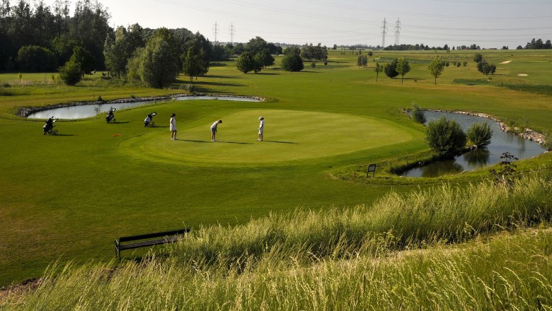 Golfers on a green golf course with a pond and trees in the background.