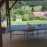 Table tennis table under a carport with a view of a green garden and hills in the background.