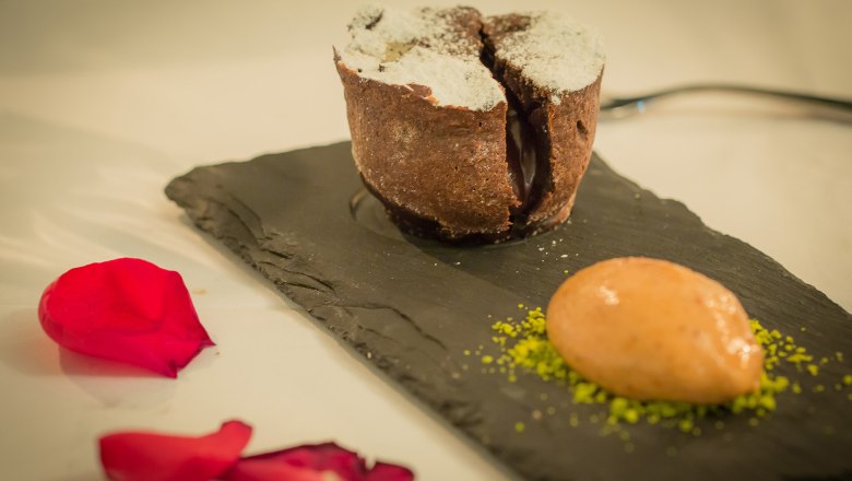 A chocolate volcano dessert on a slate plate with a scoop of ice cream and red rose petals.