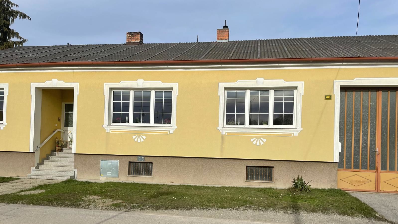 Exterior view of a yellow house with white window frames and an entrance staircase.