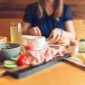 Breakfast table with cold cuts, cheese, egg, fruit and drinks, woman in the background.