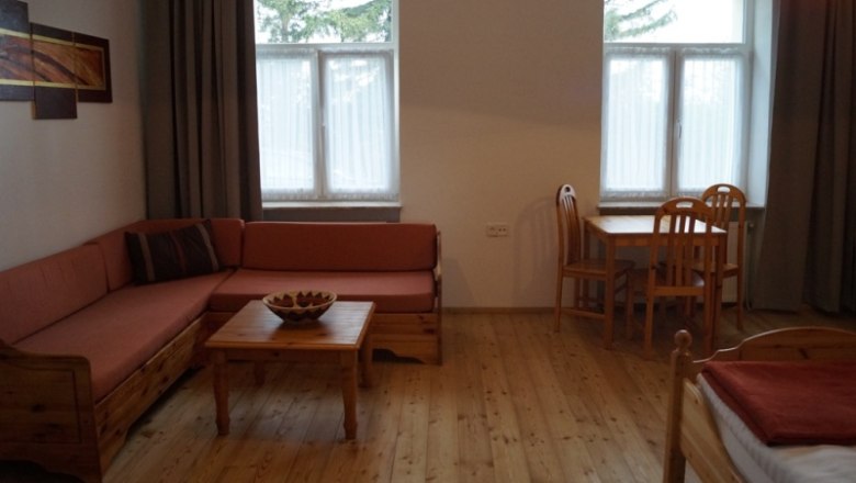 Cozy room with wooden furniture, sofa, table and chairs, two windows and a picture on the wall.
