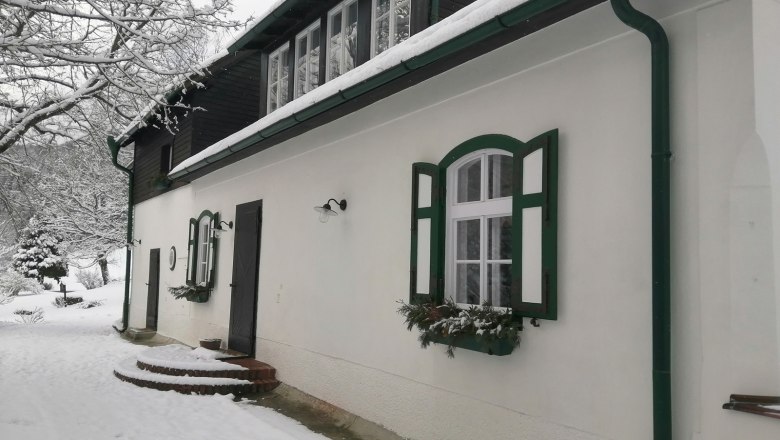 A snow-covered house with green shutters and guttering.