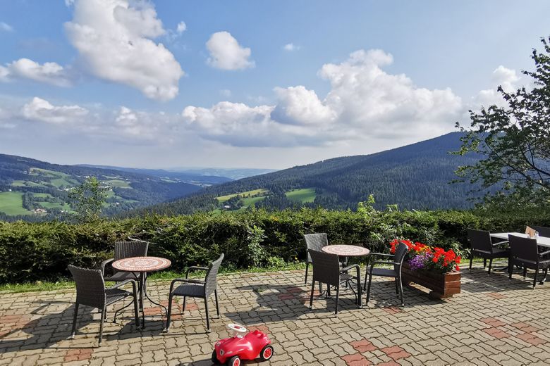 Terrace with tables and chairs, view of green hills and blue sky with clouds.