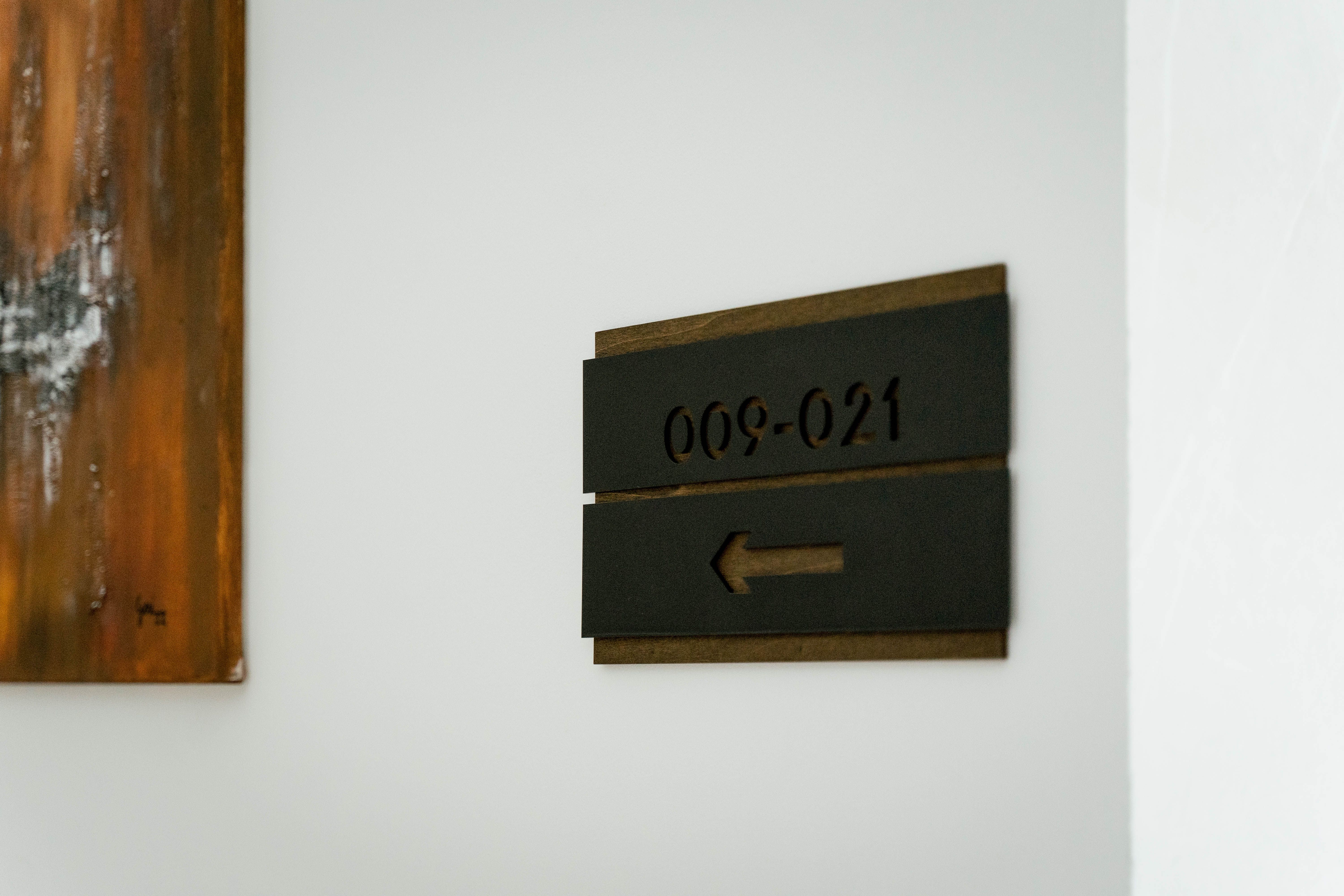 A sign with the inscription for room numbers '009-021' and an arrow pointing to the left on a white wall.