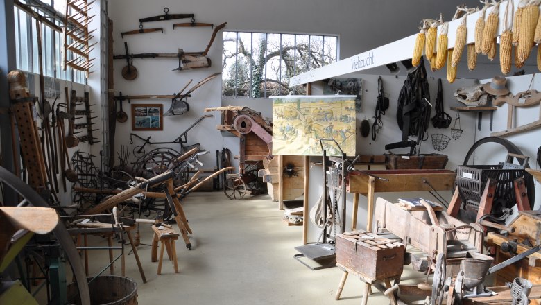 Interior view of a local history museum with old agricultural equipment and tools on the walls and floor.