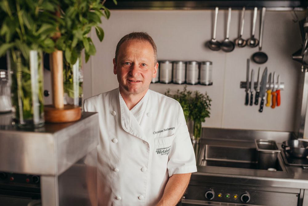 A chef in a white uniform stands in a professional kitchen.