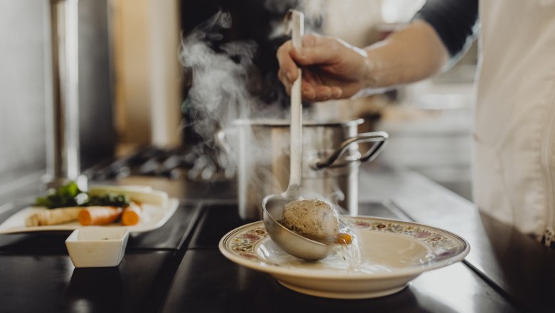 One person ladles soup with a dumpling from a pot into a plate.
