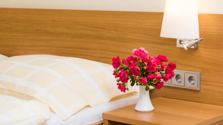 A guest room with a bed, a bedside lamp and a bouquet of flowers in a vase on the bedside table.