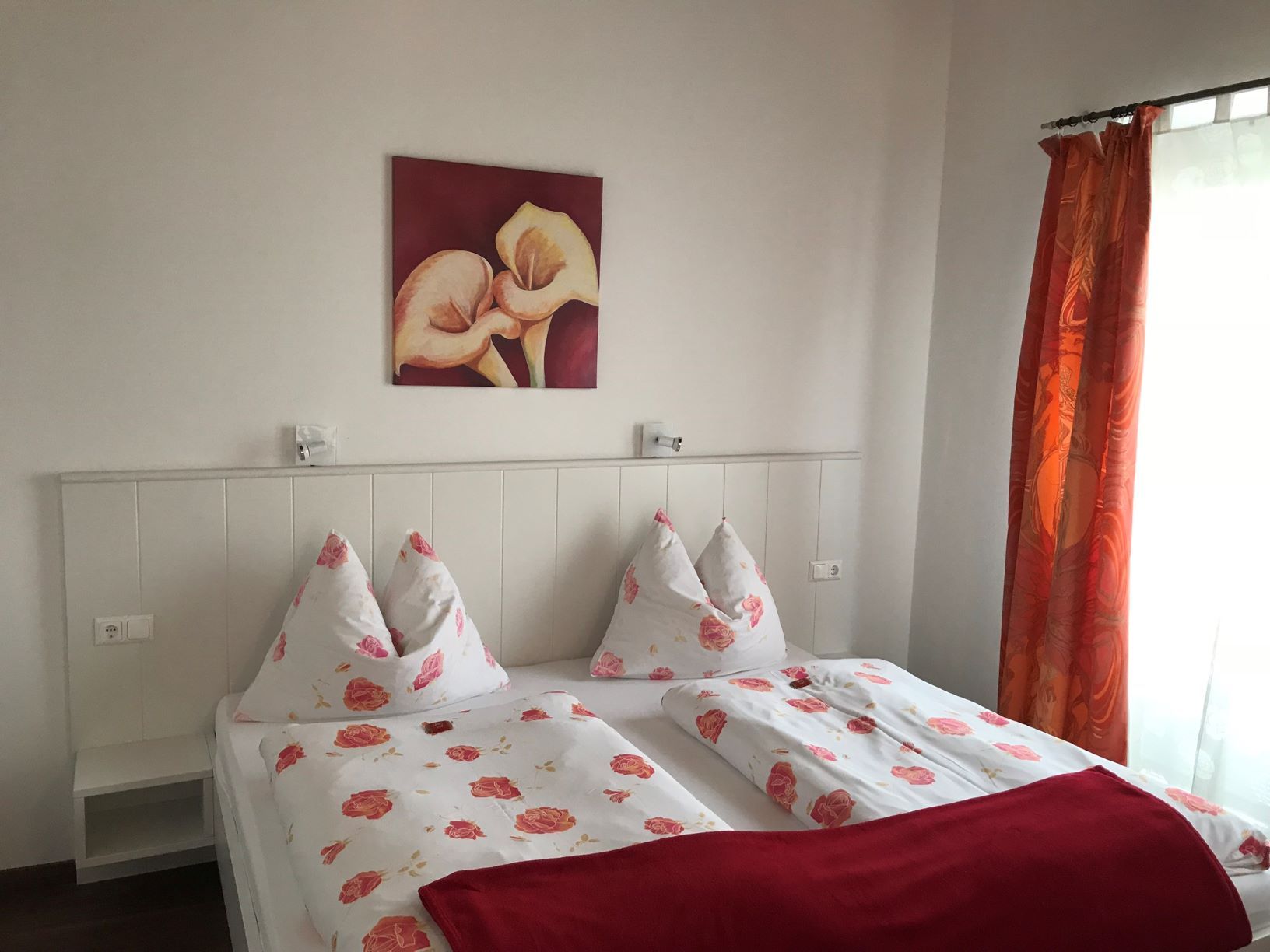 Bedroom with double bed, floral bedding, red picture and curtains.
