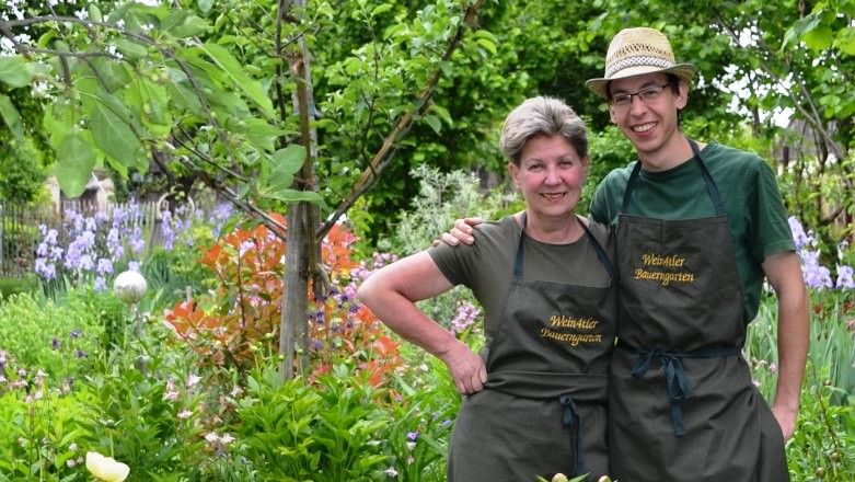 Two people in a blooming garden with aprons that say 'Weinviertler Bauerngarten' on them.