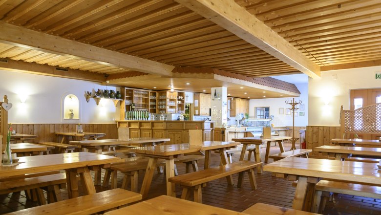 Interior view of a rustic dining room with wooden tables and benches, a bar and decorative elements on the walls.