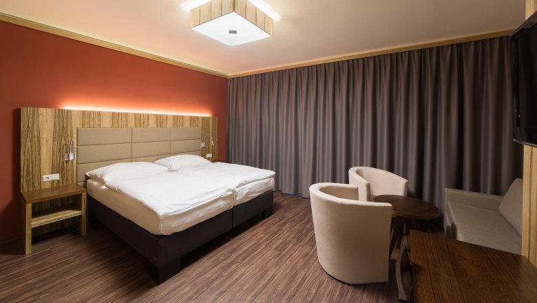 Modern hotel room with double bed, wooden furniture and curtains.