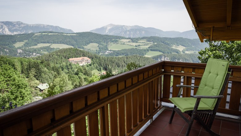 View from a balcony of a mountain landscape with forests and a building in the distance.