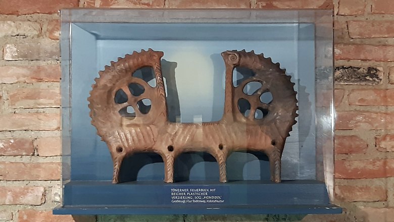 Clay figure of a fire trestle in a display case in front of a brick wall.