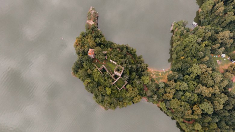 Aerial view of a wooded island with ruins and a small building on the shore of a lake.