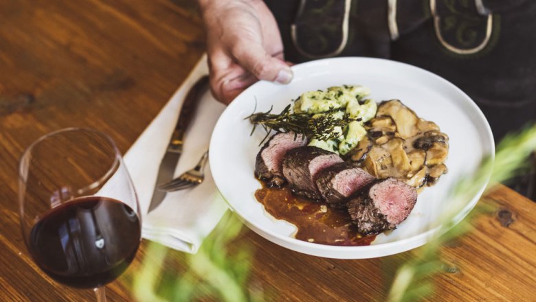 A plate of meat, mushrooms and spaetzle, with a glass of red wine next to it.