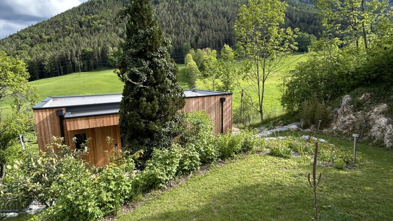 Wooden house with garden in front of a wooded hill and blue sky.