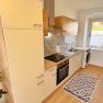 Modern kitchen with wooden and white units, stove, sink, washing machine and window. Plants and carpet as decoration.