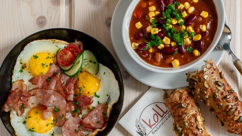 Various hot snacks on a table, including fried eggs with bacon, chili con carne, sandwiches and rolls.