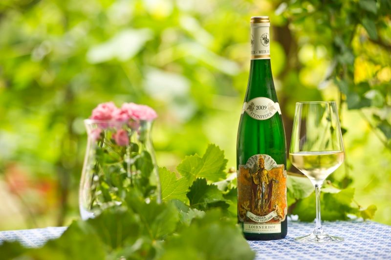 Wine bottle and glass on table with flowers and leaves in the background.