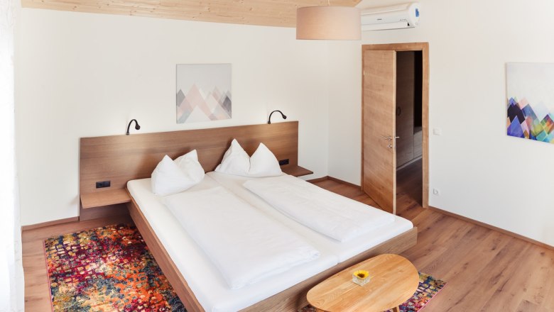 Modern bedroom with double bed, wooden furniture and colorful carpet.