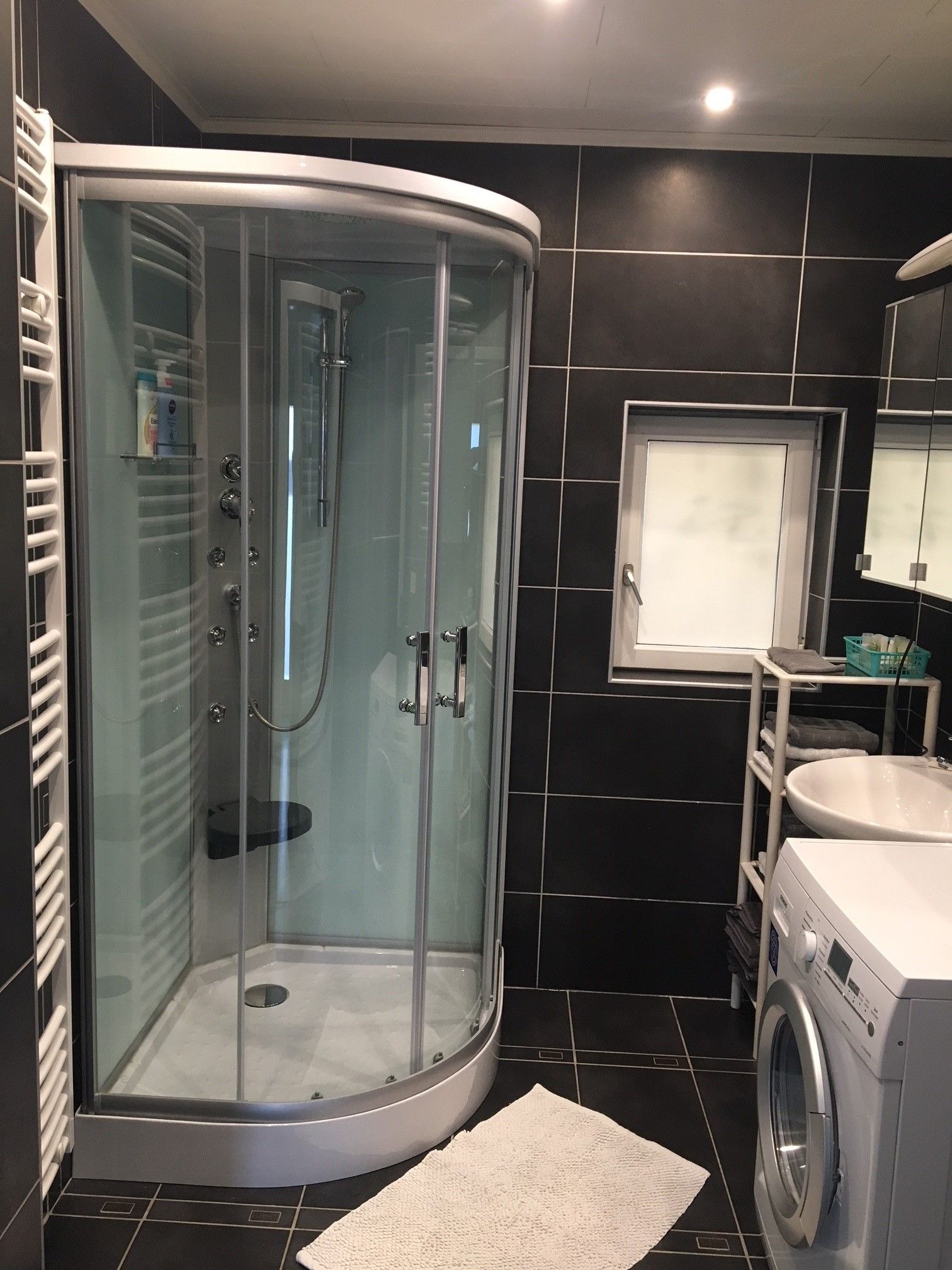 Modern bathroom with shower, washing machine and washbasin.