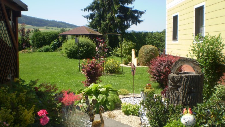 House Gerti, © Familie Hödelsberger A well-tended garden with flowers, shrubs and a yellow house in the background.