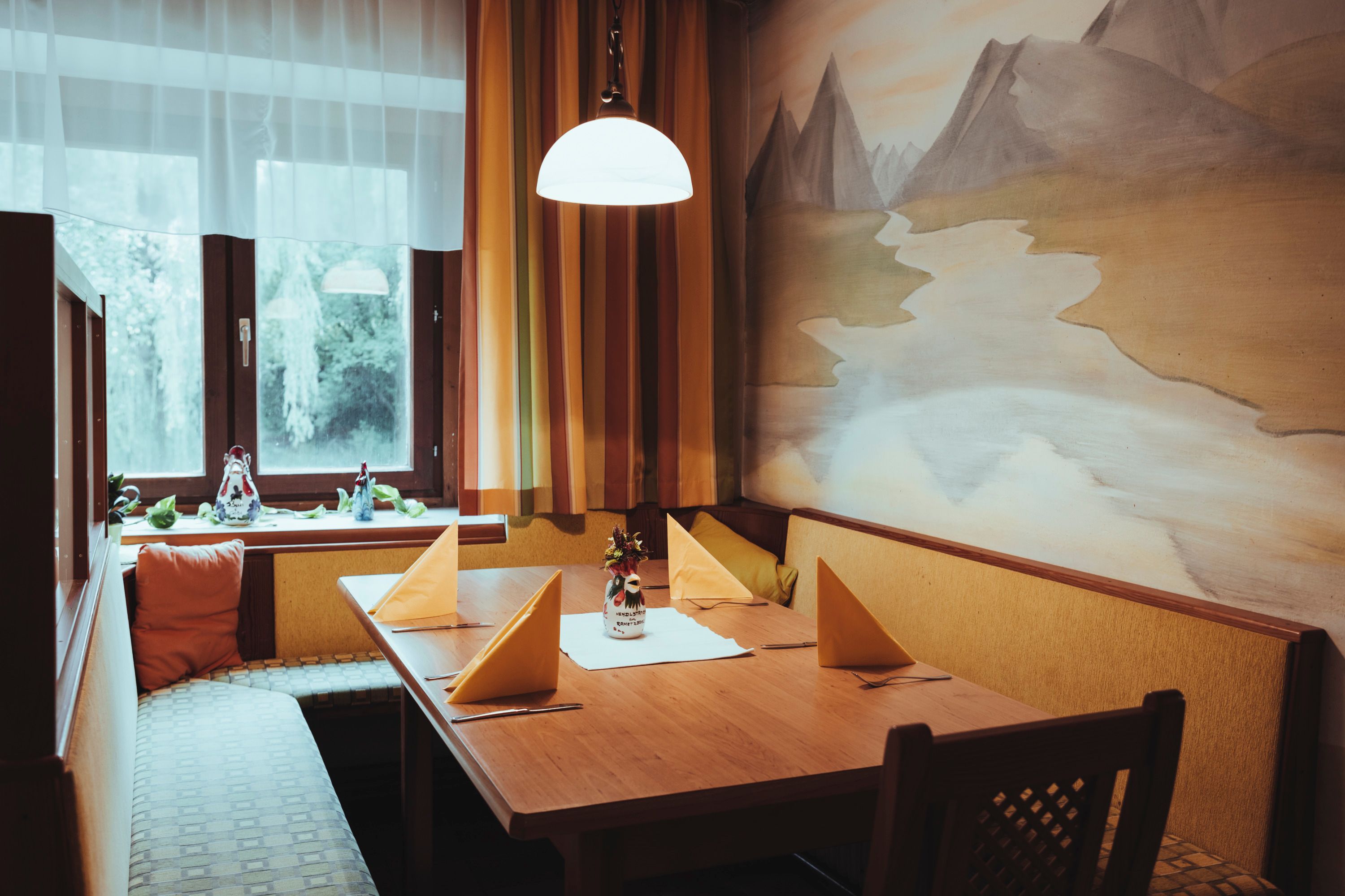 Cozy seating area with wooden table, yellow napkins and wall painting in a restaurant.
