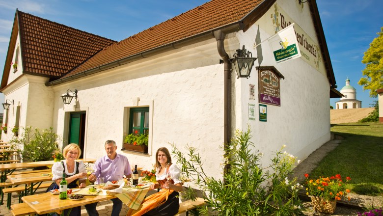 Three people sit at a table in front of a winery and enjoy a meal outdoors.