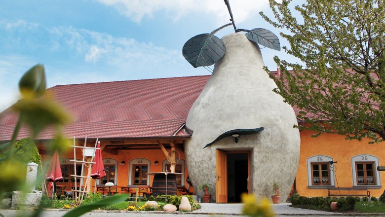 Building with pear-shaped entrance and red roof, surrounded by plants.