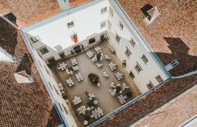 Aerial view of an inner courtyard with tables and chairs, surrounded by a building with red tiled roofs.
