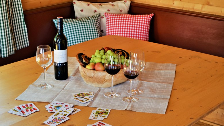 A table with wine bottle, wine glasses, fruit bowl and playing cards.