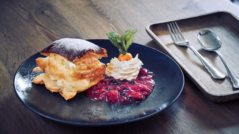 A dessert plate with a cream slice, roasted berries and whipped cream on a wooden table.