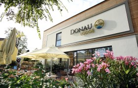 Exterior view of the Donaulodge with terrace, parasols and flowering plants.